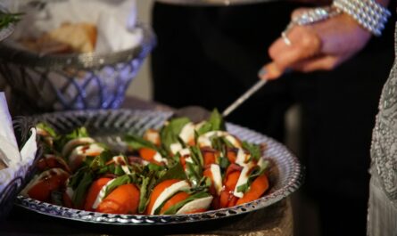 person holding stainless steel fork and knife slicing tomato on black ceramic bowl
